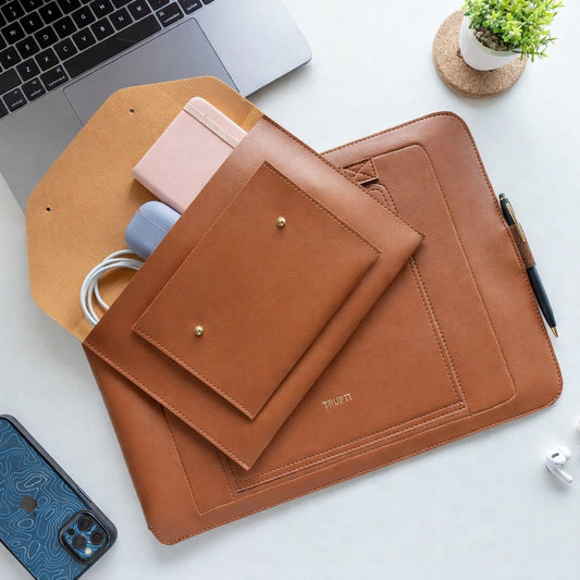 Brown leather laptop sleeve on a white surface with a laptop and phone.